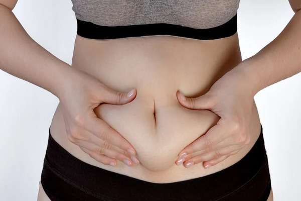 Phụ nữ trung niên dùng hai tay véo lớp mỡ quanh rốn