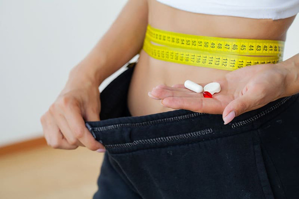 Người cầm các viên thuốc, quấn thước dây quanh eo và kéo rộng cạp quần.