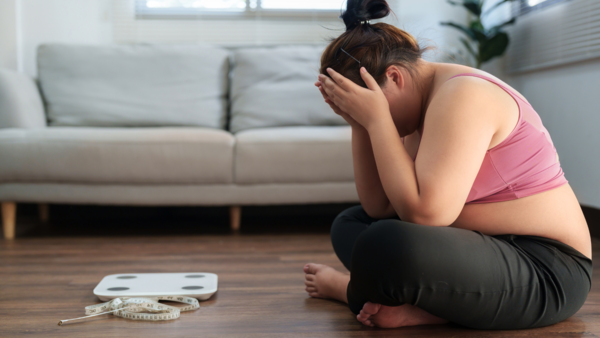 Người phụ nữ ngồi ôm đầu cạnh cân sức khỏe và thước dây.