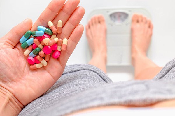 Bàn tay cầm nhiều viên thuốc khi đứng trên cân sức khỏe.